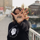 Ein Frau, die einen Humboldt-Uni Pullover trägt, hält ihr gespreizte Hand ausgestreckt in die Kamera und verdeckt so ihr Gesicht. Auf der Hand wurde mit Edding „STOP“ geschrieben. 