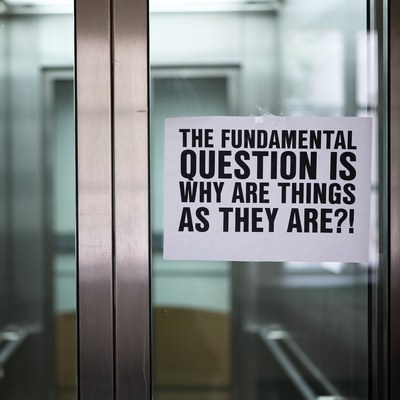 Ein Zettel hängt an einer Fahrstuhltür. Darauf steht "The fundamental question is why are things as they are?"