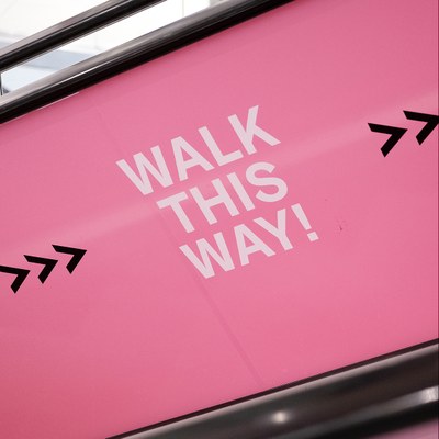 Rolltreppe mit der Seitenaufschrift (auf englisch) Walk this Way. Sowie Verlinkungen zum YouTube-Kanal der HU.