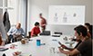 Verschiedene Personen sitzen in einem Raum und arbeiten mit Laptops