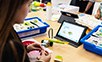 Mädchen schaut auf ein tablet und bastelt mit Legosteinen