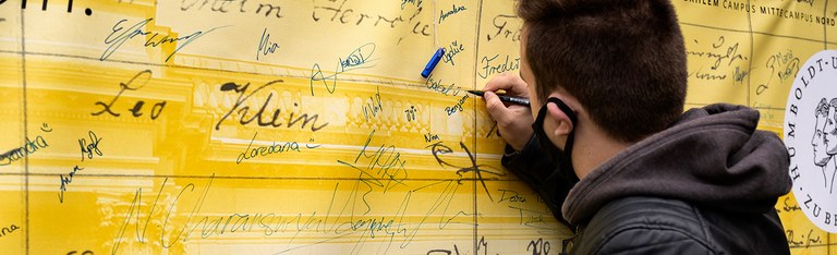 Willkommen an der HU - Studierender unterschreibt Wand