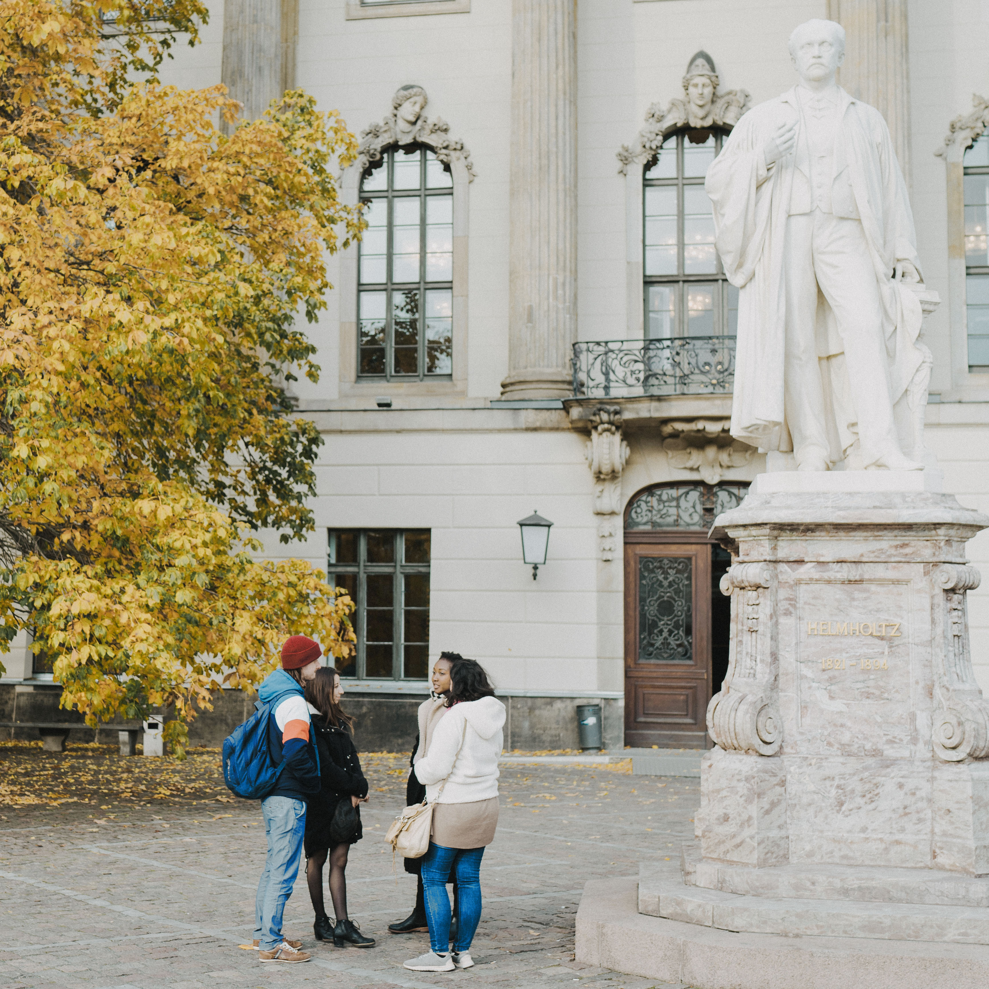 Vier Studierende stehen vor dem Hauptgebäude der Humboldt-Universität und unterhalten sich.