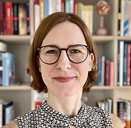 Jule Specht in einem Büro, im Hintergrund ist ein Bücherschrank. Jule Specht schaut in die Kamera