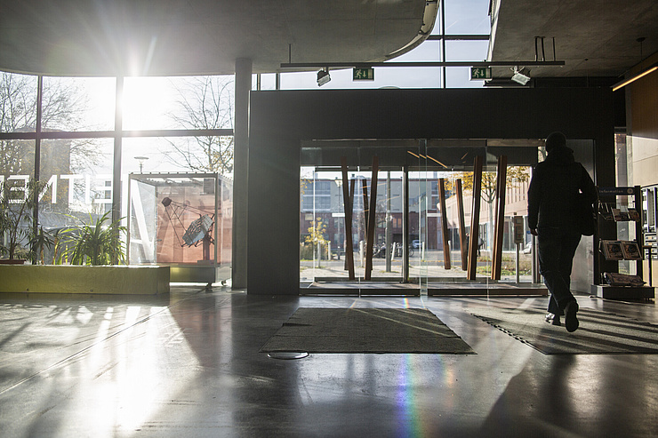 Silhouette eines Menschen der durch das sonnendurchflutete Foyer des Instituts für Physik auf dem HU-Campus Adlershof läuft.