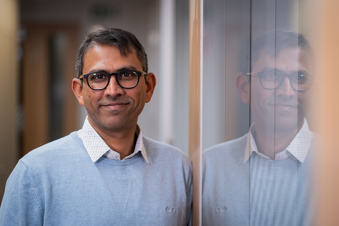 Bharath Ananthasubramania Dr. Bharath Ananthasubramaniam leht an einem Glaswand, die sein Gesicht spiegelt.