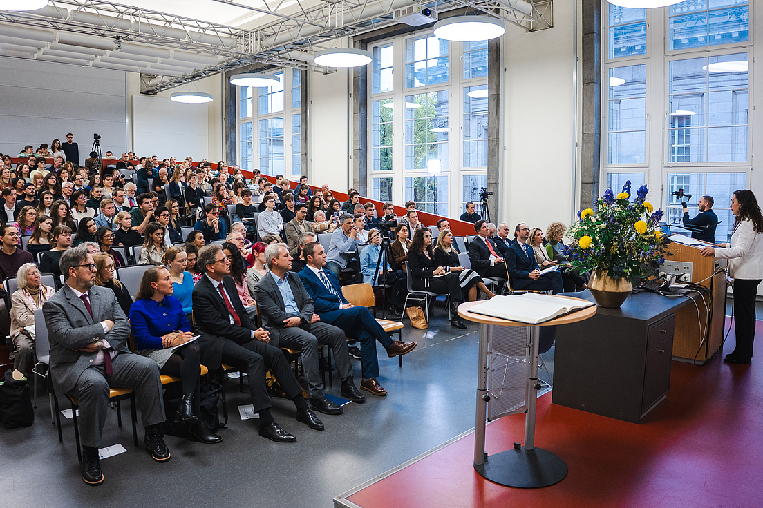 Dr. Vjosa Osmani-Sadriu spricht an einem Rednerpult vor einem gefüllten Saal. Das Publikum besteht vor allem aus Studierenden.