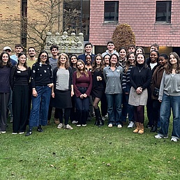 Group photo of young people standing on green grass. A brown building in the background.