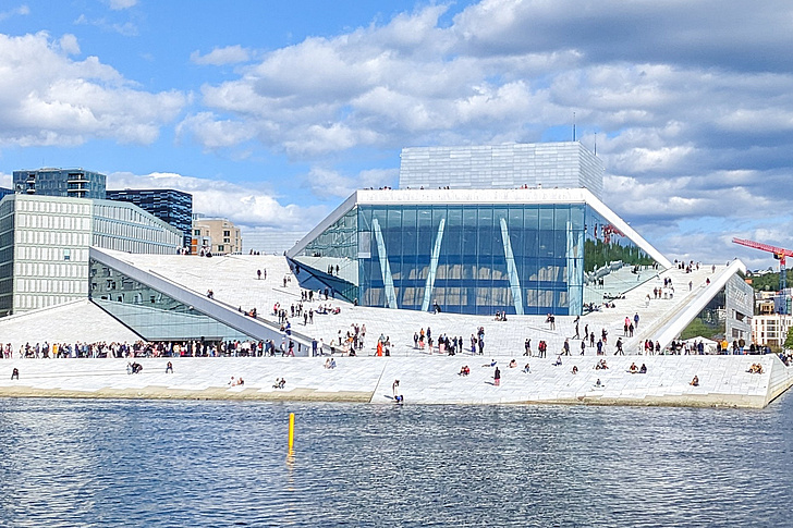 Modernes Gebäude mit schrägen, weißen Fassadenflächen und vielen Menschen auf den geneigten Flächen am Wasser