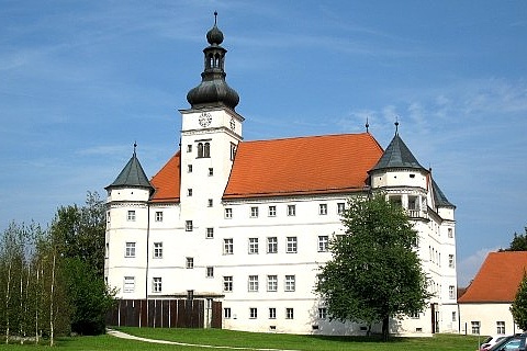 Schloss Hartheim mit blauem Himmel, weißen Fassaden und rotem Ziegeldach. 
