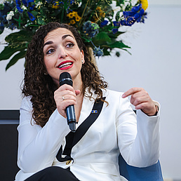 Vjosa Osmani-Sadriu wie sie auf einem Stuhl sitzend eine Frage aus dem Publikum beantwortet.