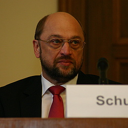Martin Schulz sitzt und schaut an der Kamera vorbei. Im unteren rechten Bildrand befindet sich ein Namensschild mit Schulz' Namen.