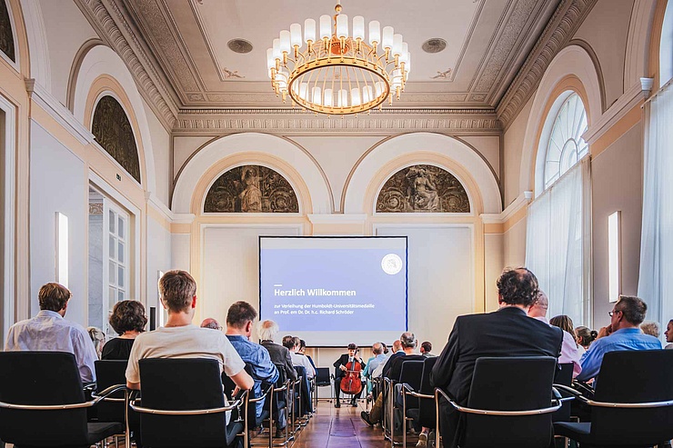 Personen sitzen im historischen Luisenfestsaal der HU und lauschen einem Cello-Spieler