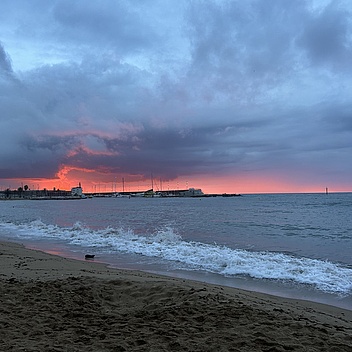 Strand mit Wellen und bewölktem Himmel bei Sonnenuntergang mit rotem Horizont