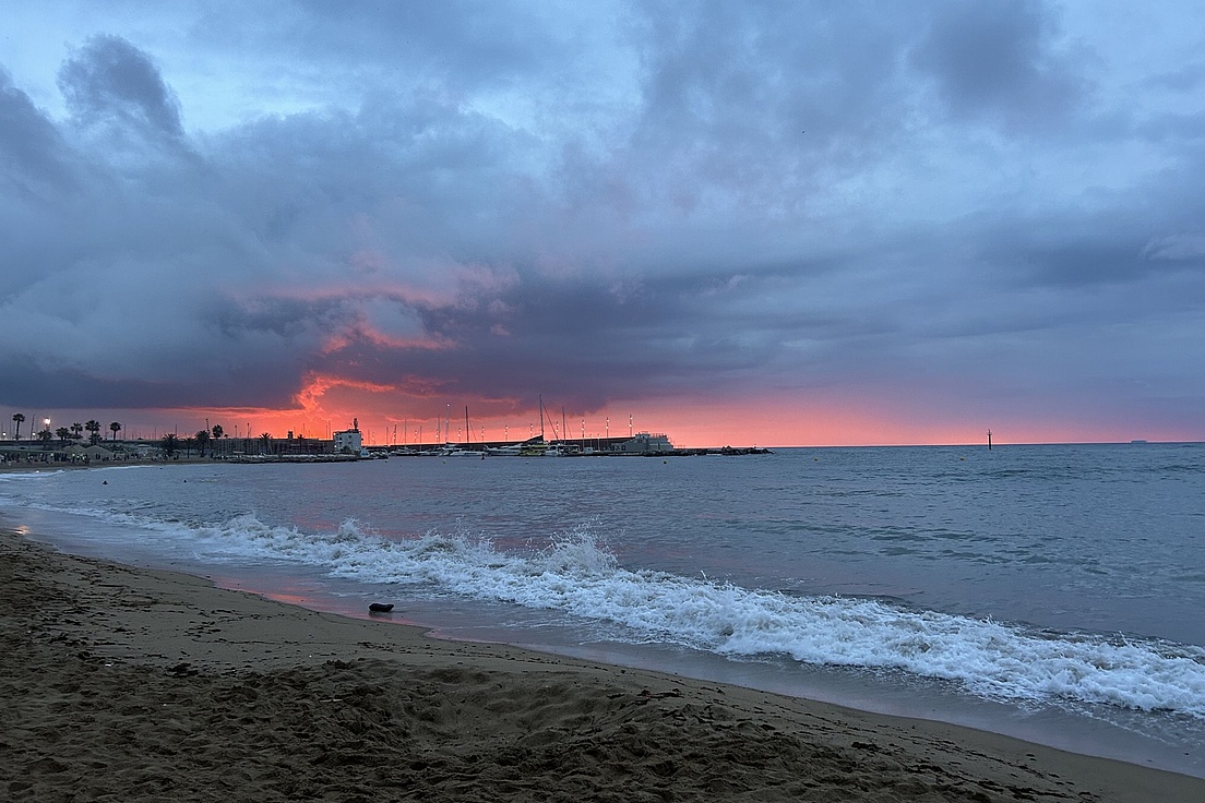 Strand mit Wellen und bewölktem Himmel bei Sonnenuntergang mit rotem Horizont