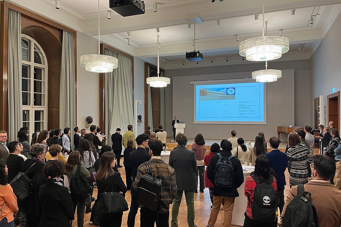 A group of young researchers in a large hall listen to the speech given by the Vice-President of HU.