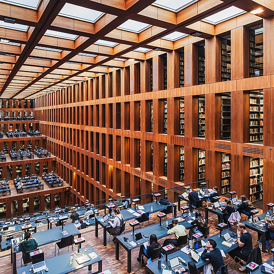 Universitätsbibliothek Studierende arbeiten an Schreibtischen in einem großen Lesesaal. Im Saal gibt es mehre markante stufenförmige Arbeitsebenen.