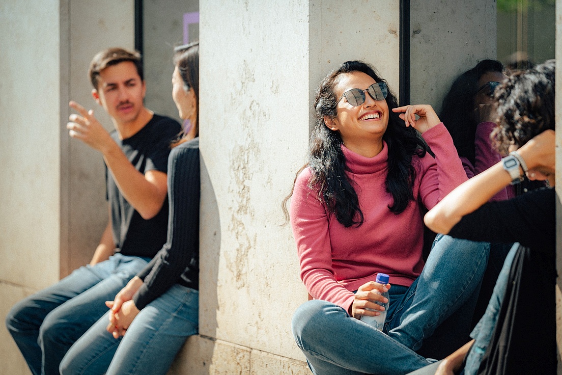 Group of students chatting outdoors, a woman in a pink sweater is smiling.