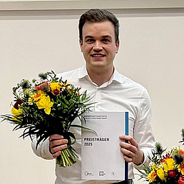 Der Preisträger des Adlershofer Dissertatiorspreises 2025 Dr. Sascha Gaudlitz (Mitte) mit den beiden ebenfalls Ausgezeichneten Dr.-Ing. Petros Beleniotis (I.) und Dr. Josefine Sprachmann. Alle haben festliche Kleidung an, einen Blumenstrauß in der rechten Hand und die Urkunde in der linken Hand.