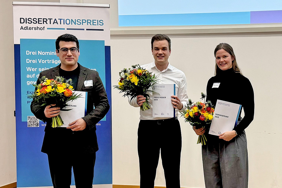 Dissertationspreis 2025 Preistraeger*iinnen Der Preisträger des Adlershofer Dissertatiorspreises 2025 Dr. Sascha Gaudlitz (Mitte) mit den beiden ebenfalls Ausgezeichneten Dr.-Ing. Petros Beleniotis (I.) und Dr. Josefine Sprachmann. Alle haben festliche Kleidung an, einen Blumenstrauß in der rechten Hand und die Urkunde in der linken Hand.