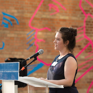 Eine Studentin spricht an einem Rednerpult. Die Wand im Hintergrund bildet in rot-blau die Köpfe der Humboldt-Brüder ab.