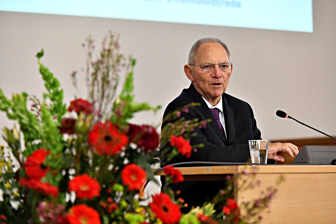 Wolfgang Schäuble am Pult, wie er seine Rede hält. In der linken Bildseite befindet sich ein Blumenstrauß.