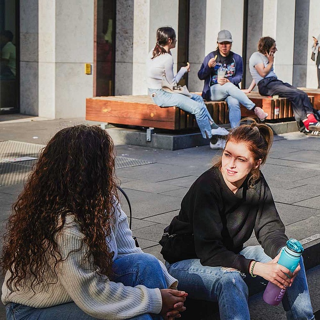 Mehre Studierende sitzen vor dem Grimm-Zentrum der HU und unterhalten sich, telefonieren oder lesen auf dem Handy. Mehre Studierende sitzen vor dem Grimm-Zentrum der HU und unterhalten sich, telefonieren oder lesen auf dem Handy.