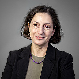 Artemis Alexiadou in einer professionellen Porträtaufnahme vor einem einfarbigen, neutralen Hintergrund. Der Hintergrund ist einheitlich grau und wirkt durch seine gleichmäßige Beleuchtung und fehlende Details sehr sauber und minimalistisch. Dieser neutrale Hintergrund lenkt den Fokus vollständig auf die Person im Vordergrund und unterstreicht den formellen Charakter des Bildes.