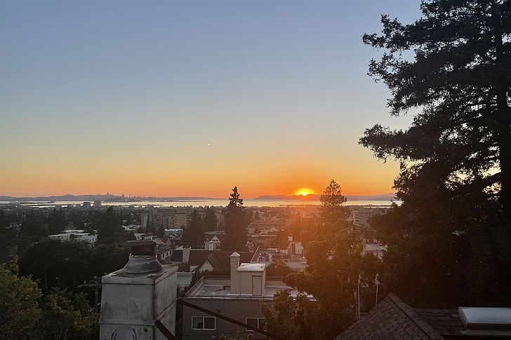 Sonnenuntergang über einer Stadt mit Häusern, Bäumen und Bergen am Horizont