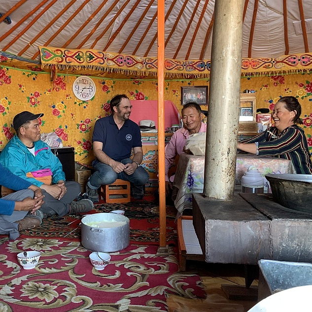 Gruppe von Personen sitzt in einer bunt dekorierten traditionellen Jurte und unterhält sich.