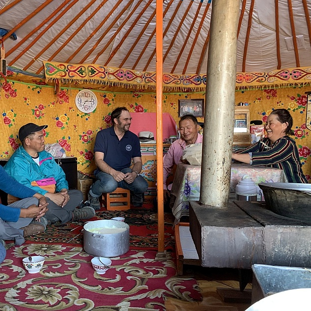 Group of people sitting in a colorful, traditionally decorated yurt, engaging in conversation.