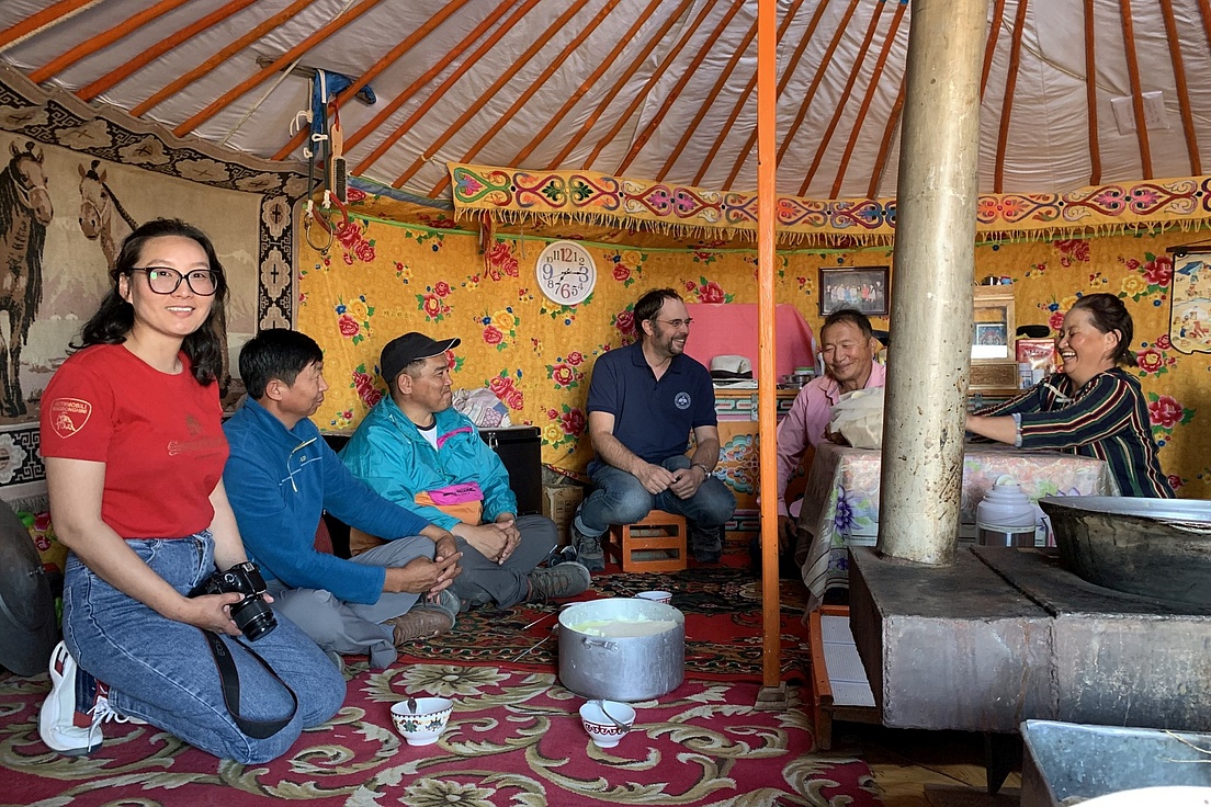 Group of people sitting in a colorful, traditionally decorated yurt, engaging in conversation.