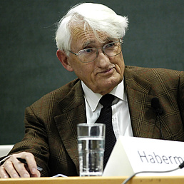Jürgen Habermas An elderly man with white hair and glasses is sitting at a table with a microphone and a name badge.