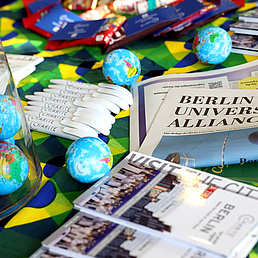 Ein Tisch mit Flyern der Berlin University Alliance mit bunten Spielzeug Globen.