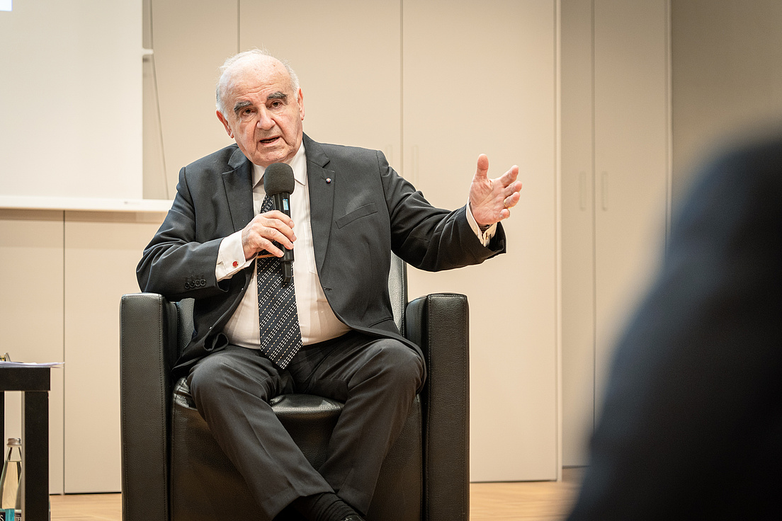George Vella wie er auf einem Stuhl sitzend eine Frage aus dem Publikum beantwortet.