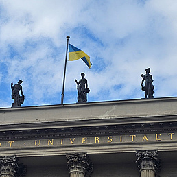 Die Ukraine-Fahne weht auf dem HU-Hauptgebäude. Im Hintergrund blauer Himmel und Wolken.