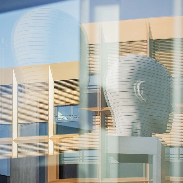 Die Köpfe des Kunstwerkes "Kopfbewegung - heads, shifting" spiegeln sich in einem Fenster in der Forschungsstadt Adlershof.
