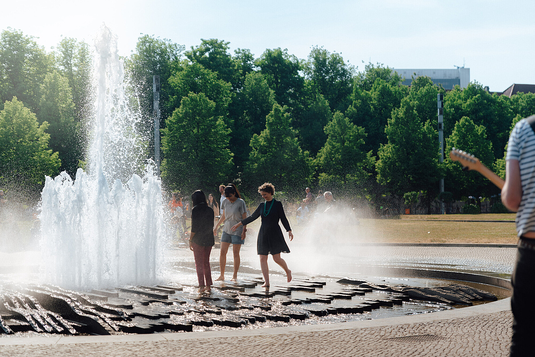 Drei Personen, die sich an einer großen Wasserfontäne abkühlen.