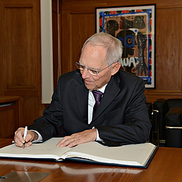 Wolfgang Schäuble sitzt am Tisch und schreibt in ein vor ihm ausgebreitetes Buch.