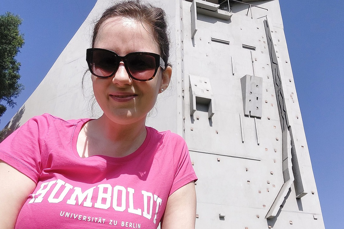 Frau mit rosa T-Shirt mit der Aufschrift 'HUMBOLDT UNIVERSITÄT ZU BERLIN' vor einer Kletterwand im Freien