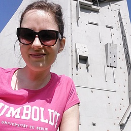 Frau mit rosa T-Shirt mit der Aufschrift 'HUMBOLDT UNIVERSITÄT ZU BERLIN' vor einer Kletterwand im Freien