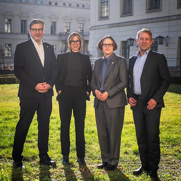 Das Präsidium der Humboldt-Universität zu Berlin Die vier Mitglieder des Präsidiums der HU stehen nebeneinander auf einer Wiese. Im Hintergrund Gebäude der HU.