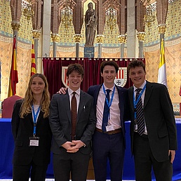 Photo of three young men and a young woman in costumes. In the background, the apse of a church.