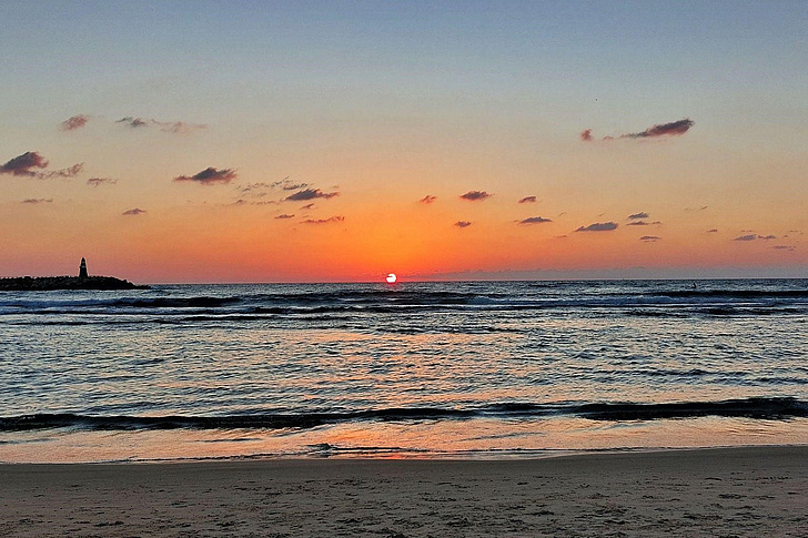 Sonnenuntergang über dem Meer mit leicht bewölktem Himmel und Sandstrand im Vordergrund