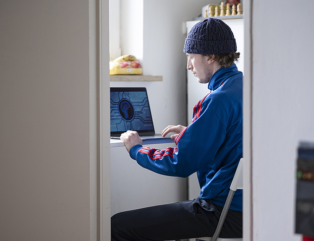 Digitale Lehre: Computerarbeitsplatz Ein Student arbeitet an einem Bibliotheks-Schreibtisch mit Laptop und großem Computer-Bildschirm.