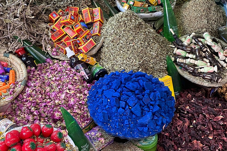 Marktstand mit verschiedenen losen Gewürzen und getrockneten Blüten, darunter ein großer Haufen blauer Kristalle in der Mitte