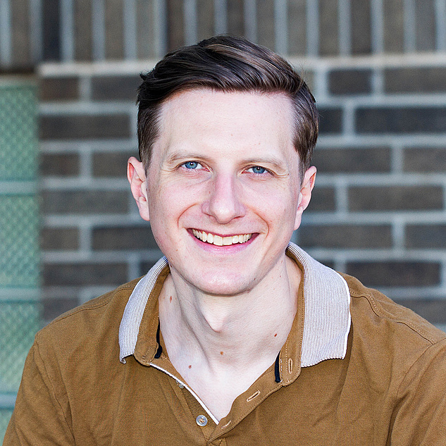 Torben Ott Torben Ott mit kurzen, dunkelbraunen Haaren und blauen Augen lächelt freundlich in die Kamera. Er trägt ein braunes Polohemd mit einem hellen, gestreiften Kragen. Der Hintergrund besteht aus einer grauen Ziegelwand.