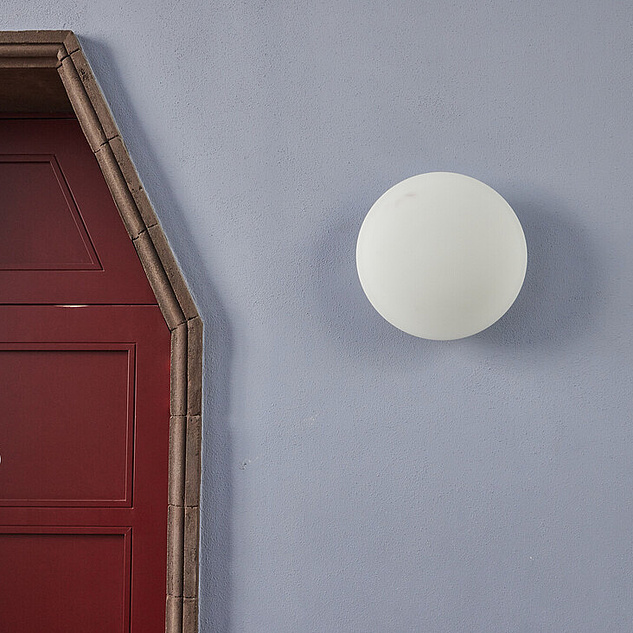 Einen Wand mit einer weißen, runden Wandlampe. Daneben eine rote Tür mit Holzrahmen. 