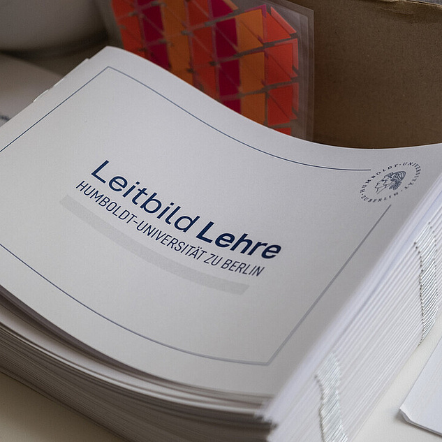 Ein Tisch mit einem Stapel an Broschüren auf denen Leitbild Lehre steht.