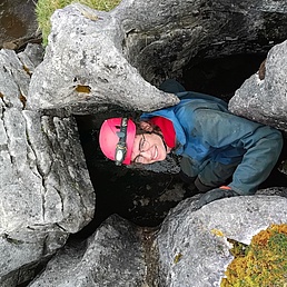 Mann mit rosa Helm und Stirnlampe klettert in engen Felsen mit Moos bei Caving-Abenteuer